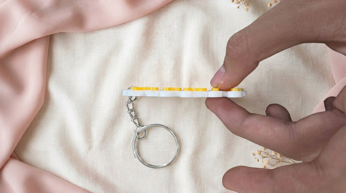 Handheld edge view of Yellow NameLoop name keychain showing its white backing