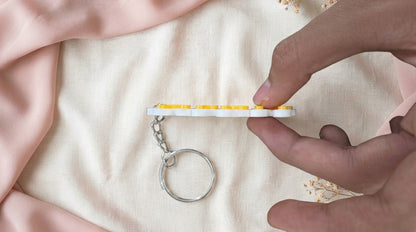 Handheld edge view of Yellow NameLoop name keychain showing its white backing